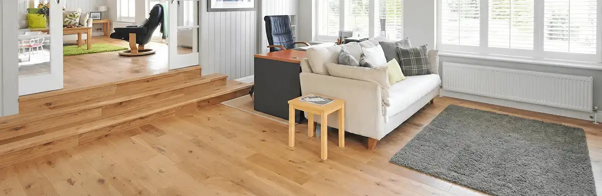 A modern living room with professionally installed laminate flooring, a beige sofa, a small side table, a gray rug, and large windows with white shutters in Tucson, AZ